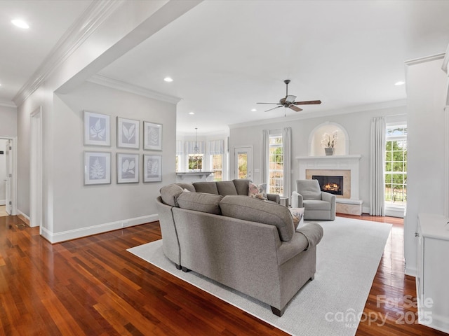 living room with dark wood-type flooring, ornamental molding, a ceiling fan, a glass covered fireplace, and recessed lighting