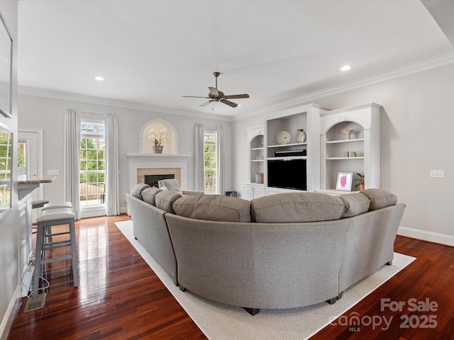 living area featuring baseboards, ceiling fan, ornamental molding, a fireplace, and dark wood-style floors