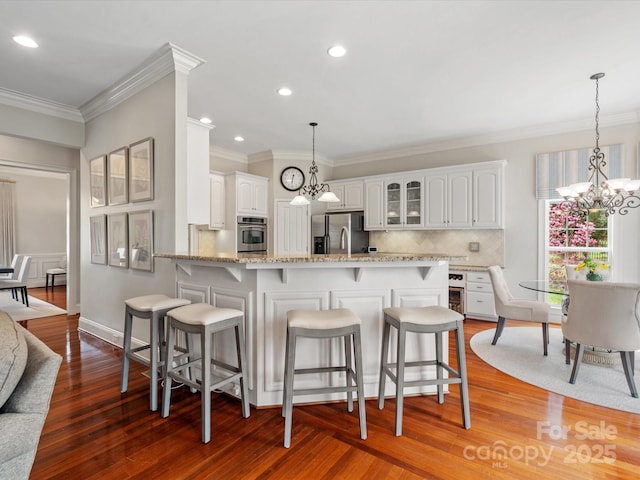 kitchen featuring glass insert cabinets, a peninsula, a kitchen breakfast bar, a notable chandelier, and stainless steel appliances