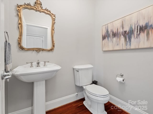 bathroom featuring toilet, wood finished floors, baseboards, and a sink