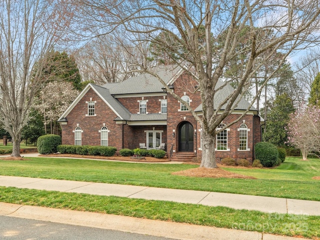 traditional-style home with brick siding, roof with shingles, and a front yard