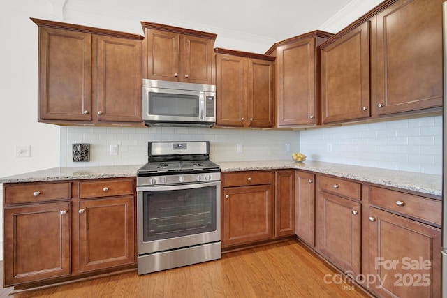 kitchen featuring light wood-style flooring, light stone counters, tasteful backsplash, and appliances with stainless steel finishes