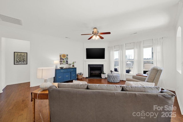 living room featuring visible vents, a fireplace with flush hearth, hardwood / wood-style flooring, baseboards, and ceiling fan