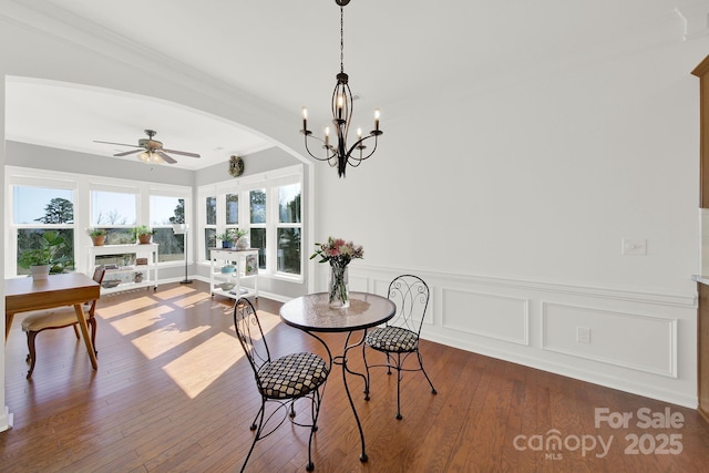 dining space featuring a wealth of natural light, ceiling fan with notable chandelier, wood-type flooring, and wainscoting