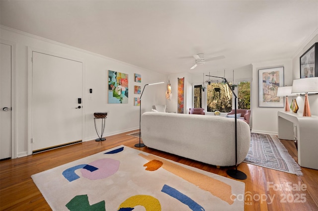 living area with baseboards, wood finished floors, a ceiling fan, and crown molding