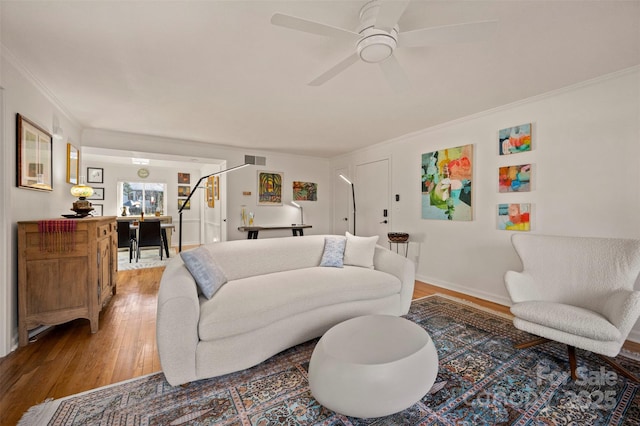 living room with visible vents, wood finished floors, crown molding, baseboards, and ceiling fan