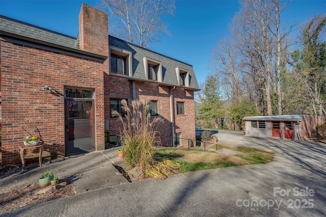 view of side of property with mansard roof, brick siding, and a chimney