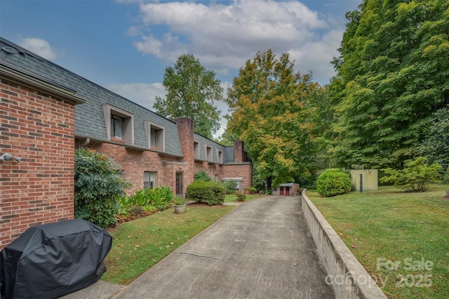 exterior space featuring mansard roof, brick siding, and a lawn