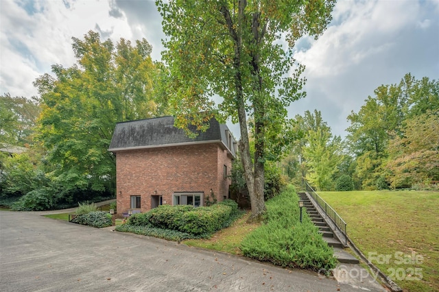 view of home's exterior featuring a lawn, mansard roof, a shingled roof, brick siding, and stairs