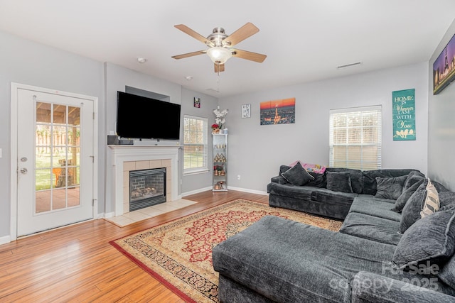 living area with visible vents, wood finished floors, baseboards, ceiling fan, and a tile fireplace