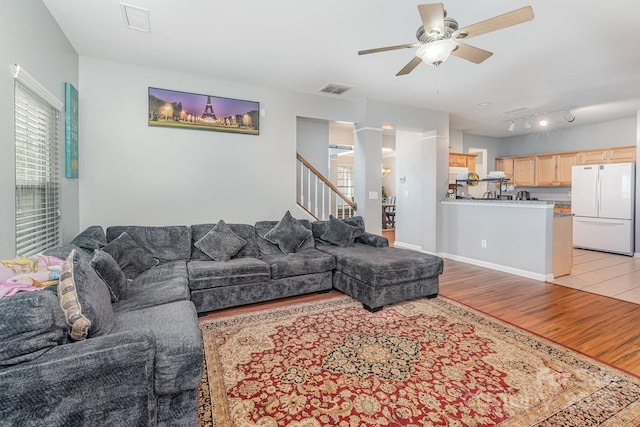 living area with visible vents, ceiling fan, baseboards, stairs, and light wood-style floors