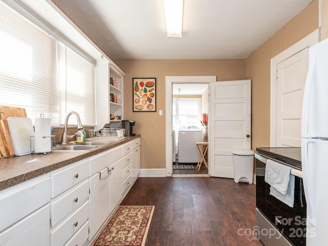 kitchen with a sink, washer / clothes dryer, dark wood finished floors, freestanding refrigerator, and white cabinets