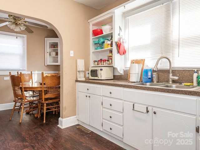 kitchen with white microwave, arched walkways, a sink, dark wood-type flooring, and white cabinets