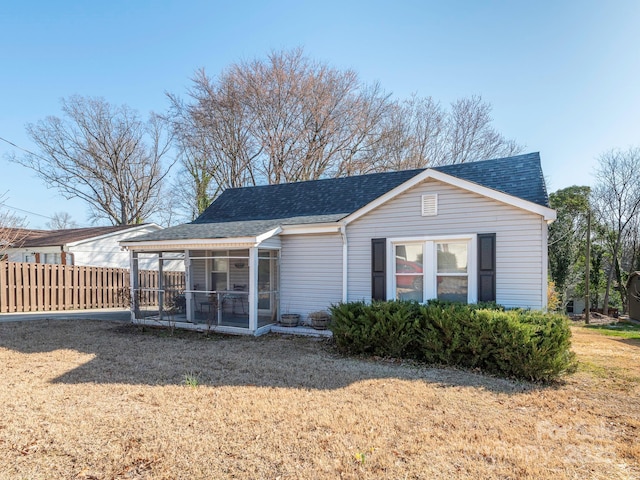 view of front of home with a front lawn, fence, a sunroom, and a shingled roof