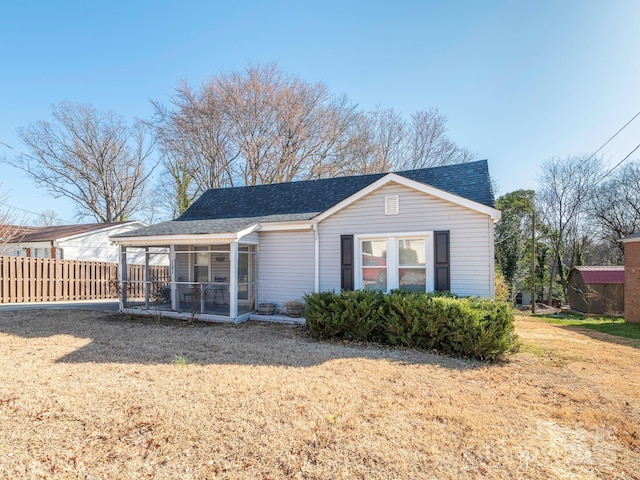 back of property with a yard, fence, a shingled roof, and a sunroom