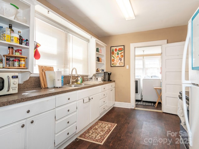 kitchen with white microwave, open shelves, dark wood-type flooring, washer and dryer, and a sink