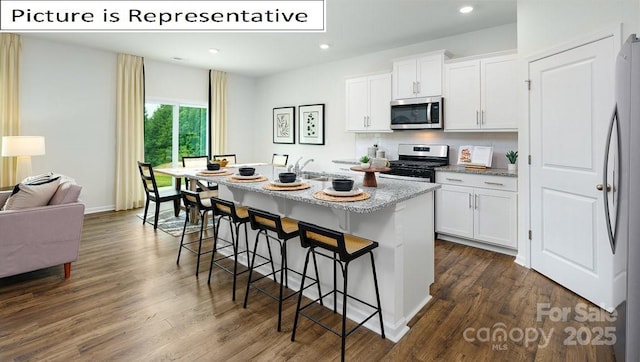 kitchen with a kitchen breakfast bar, an island with sink, dark wood-style flooring, and stainless steel appliances