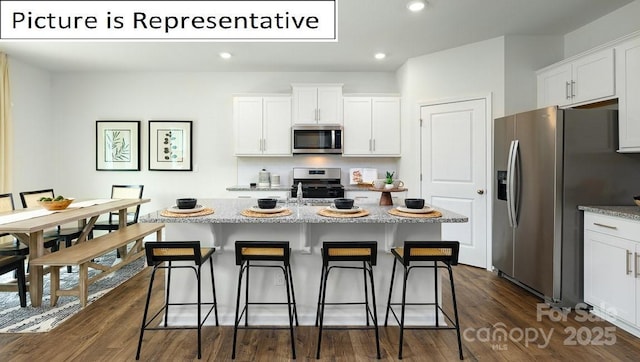 kitchen featuring dark wood-type flooring, a breakfast bar, a center island with sink, appliances with stainless steel finishes, and white cabinets