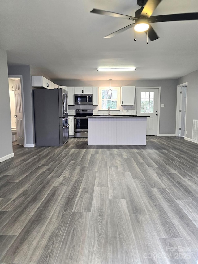 kitchen with stainless steel appliances, dark countertops, open floor plan, and white cabinetry