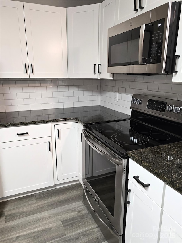 kitchen featuring backsplash, dark stone counters, stainless steel appliances, wood finished floors, and white cabinetry