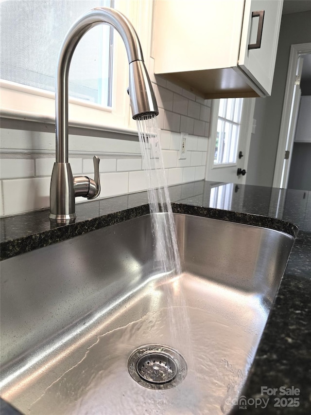 room details featuring a sink, decorative backsplash, dark stone countertops, and white cabinetry