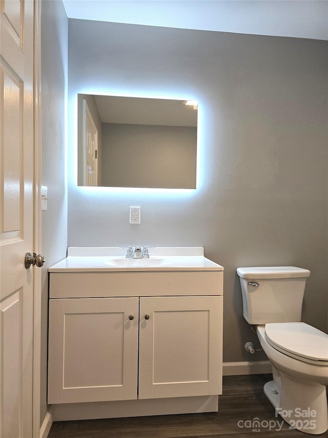 bathroom with baseboards, toilet, wood finished floors, and vanity