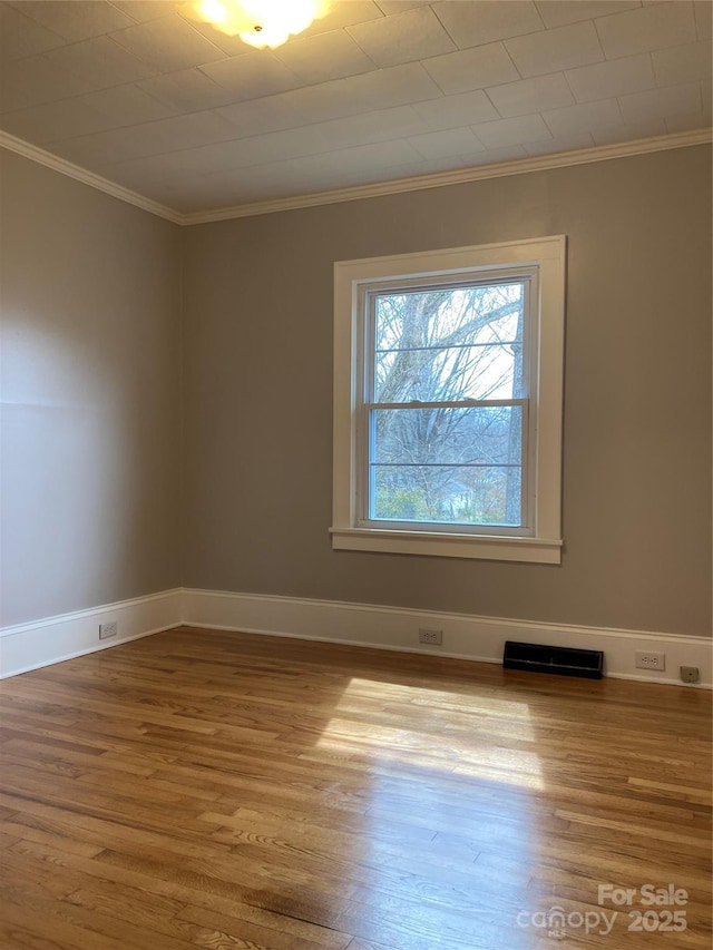 spare room with crown molding, wood finished floors, visible vents, and baseboards