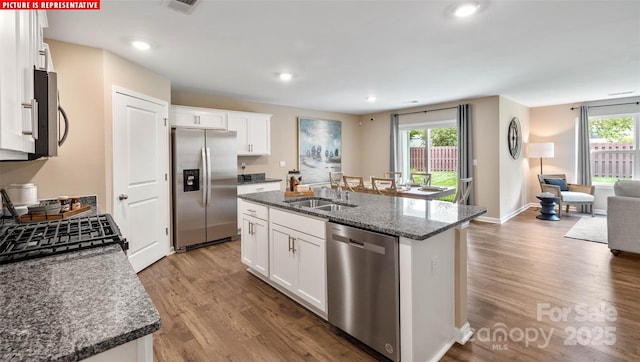 kitchen featuring a sink, a healthy amount of sunlight, wood finished floors, stainless steel appliances, and a kitchen island with sink