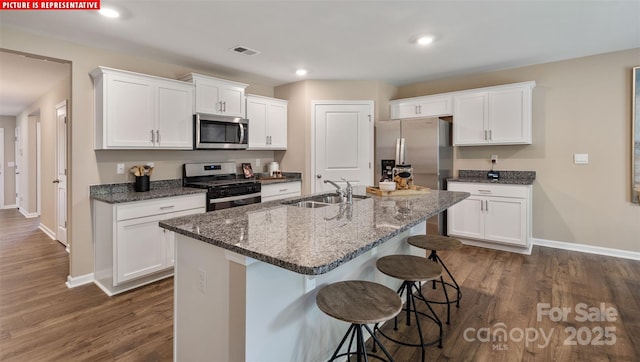 kitchen featuring visible vents, a breakfast bar, stainless steel appliances, white cabinetry, and a sink