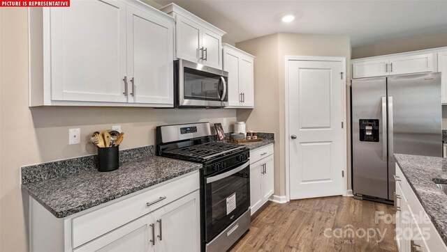 kitchen featuring dark stone countertops, stainless steel appliances, light wood-style flooring, and white cabinetry