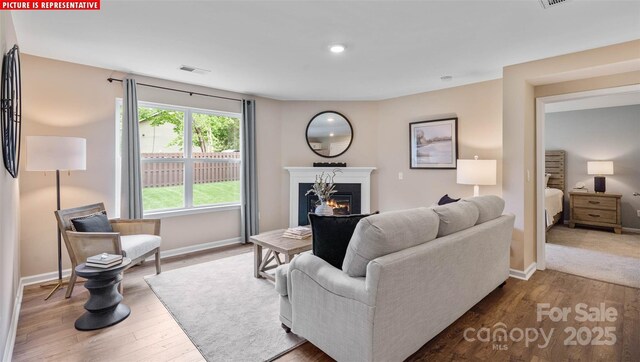 living area with wood finished floors, visible vents, a warm lit fireplace, and baseboards