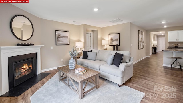 living area featuring recessed lighting, visible vents, wood finished floors, and a glass covered fireplace