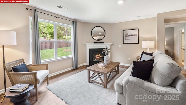 living area with visible vents, wood finished floors, baseboards, and a glass covered fireplace