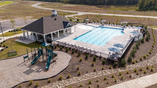 community pool with playground community, a patio, and fence