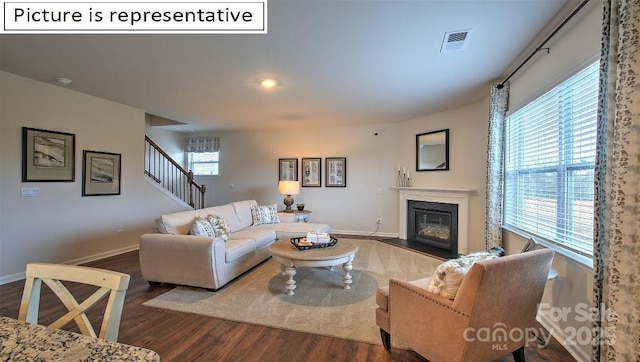 living area with wood finished floors, visible vents, baseboards, stairs, and a glass covered fireplace