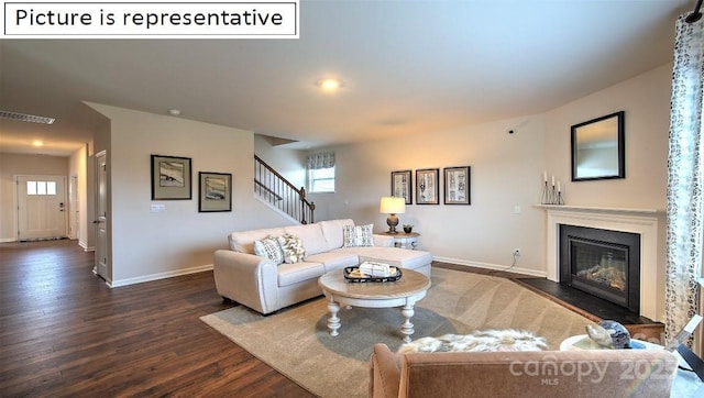 living room featuring visible vents, baseboards, stairs, a glass covered fireplace, and dark wood-style flooring