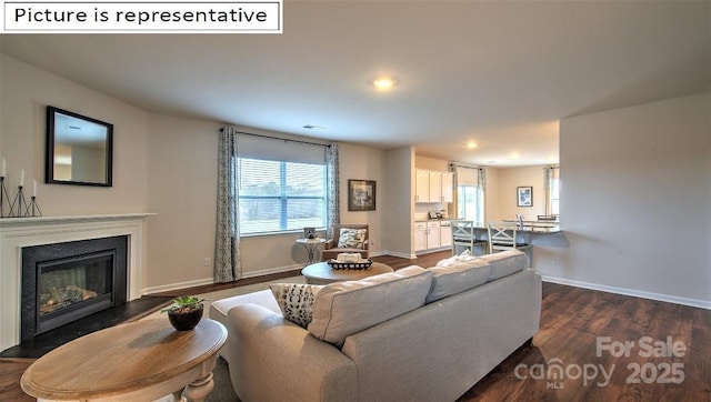 living room featuring a glass covered fireplace, recessed lighting, dark wood-style floors, and baseboards