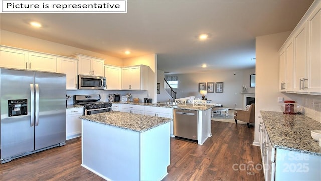 kitchen with dark wood-type flooring, light stone countertops, appliances with stainless steel finishes, a peninsula, and white cabinets