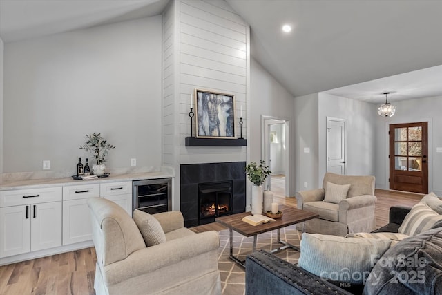 living area featuring beverage cooler, a chandelier, light wood-type flooring, a fireplace, and high vaulted ceiling