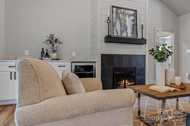 living room featuring wine cooler, lofted ceiling, light wood-style floors, and a fireplace