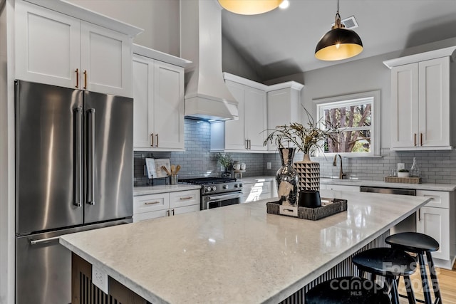 kitchen featuring high quality appliances, a sink, a kitchen bar, wall chimney exhaust hood, and tasteful backsplash