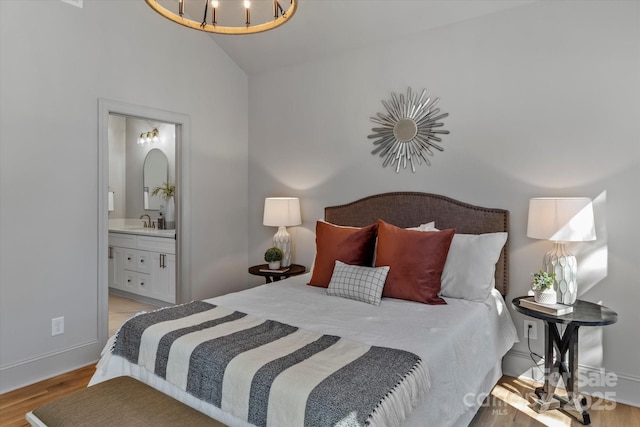 bedroom featuring wood finished floors, lofted ceiling, ensuite bath, a sink, and a chandelier