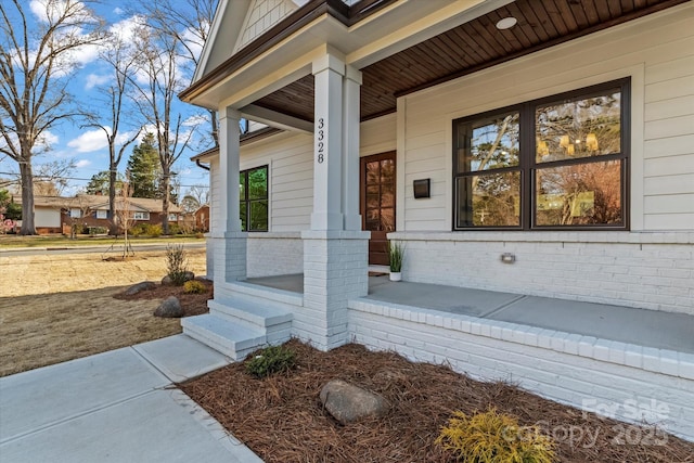 view of exterior entry featuring covered porch and brick siding