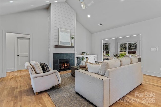 living room featuring light wood finished floors, high vaulted ceiling, visible vents, and a tiled fireplace