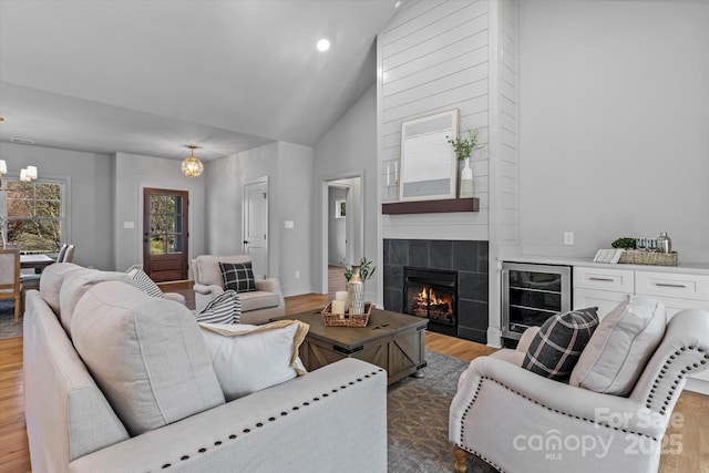 living room with high vaulted ceiling, baseboards, beverage cooler, a tiled fireplace, and wood finished floors