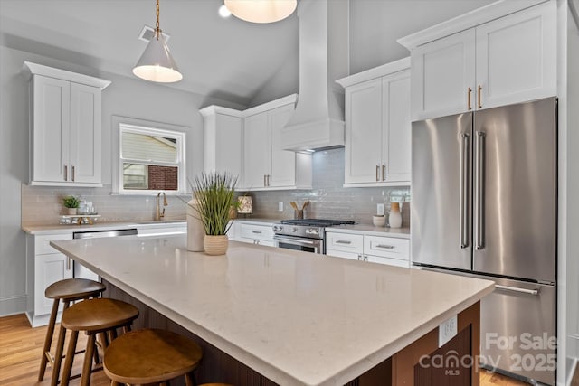 kitchen with a sink, custom range hood, white cabinets, and premium appliances