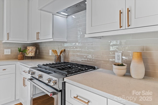 kitchen featuring backsplash, white cabinetry, light stone countertops, premium range hood, and stainless steel gas range oven