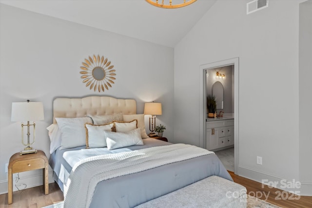 bedroom featuring visible vents, wood finished floors, ensuite bath, and vaulted ceiling