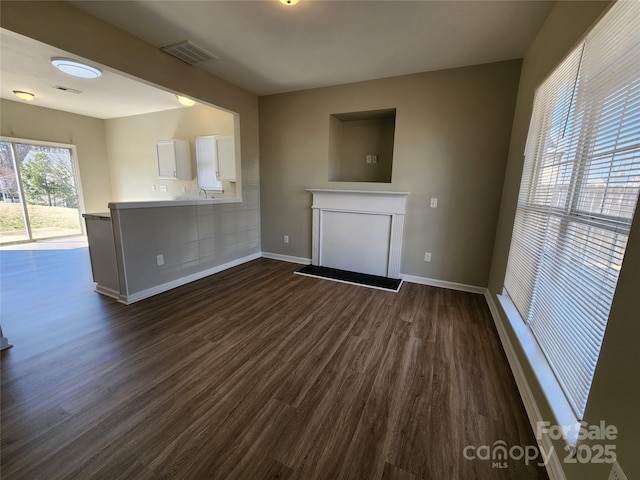 unfurnished living room featuring a fireplace, visible vents, dark wood-style flooring, and baseboards