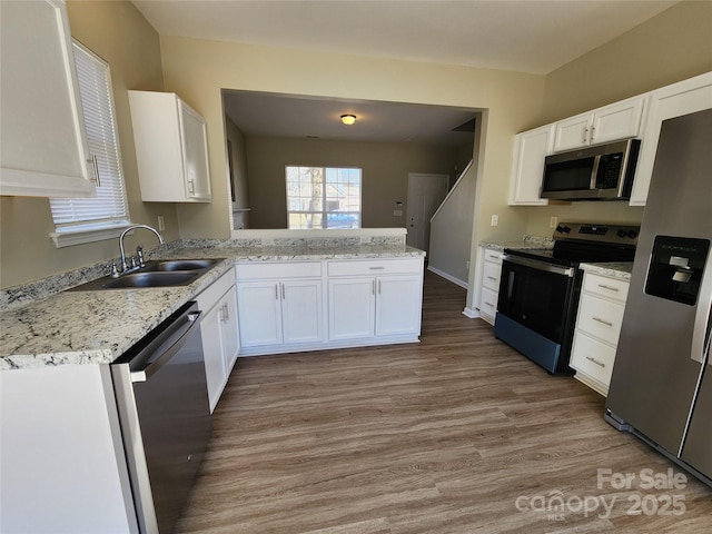 kitchen with a sink, a peninsula, appliances with stainless steel finishes, white cabinets, and light wood finished floors